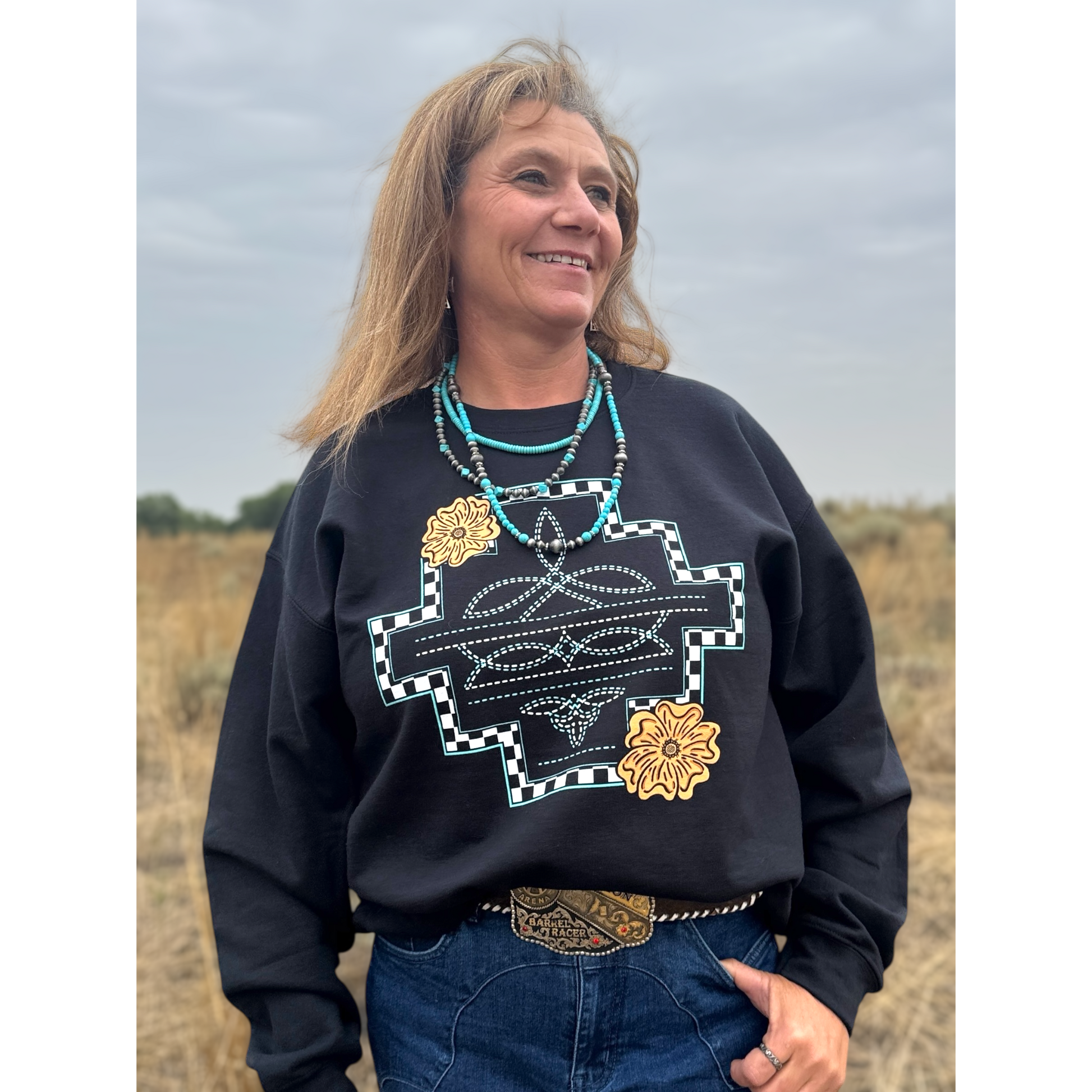 Front view of a woman wearing a western print sweatshirt with boot stitching and leather tooled flowers 