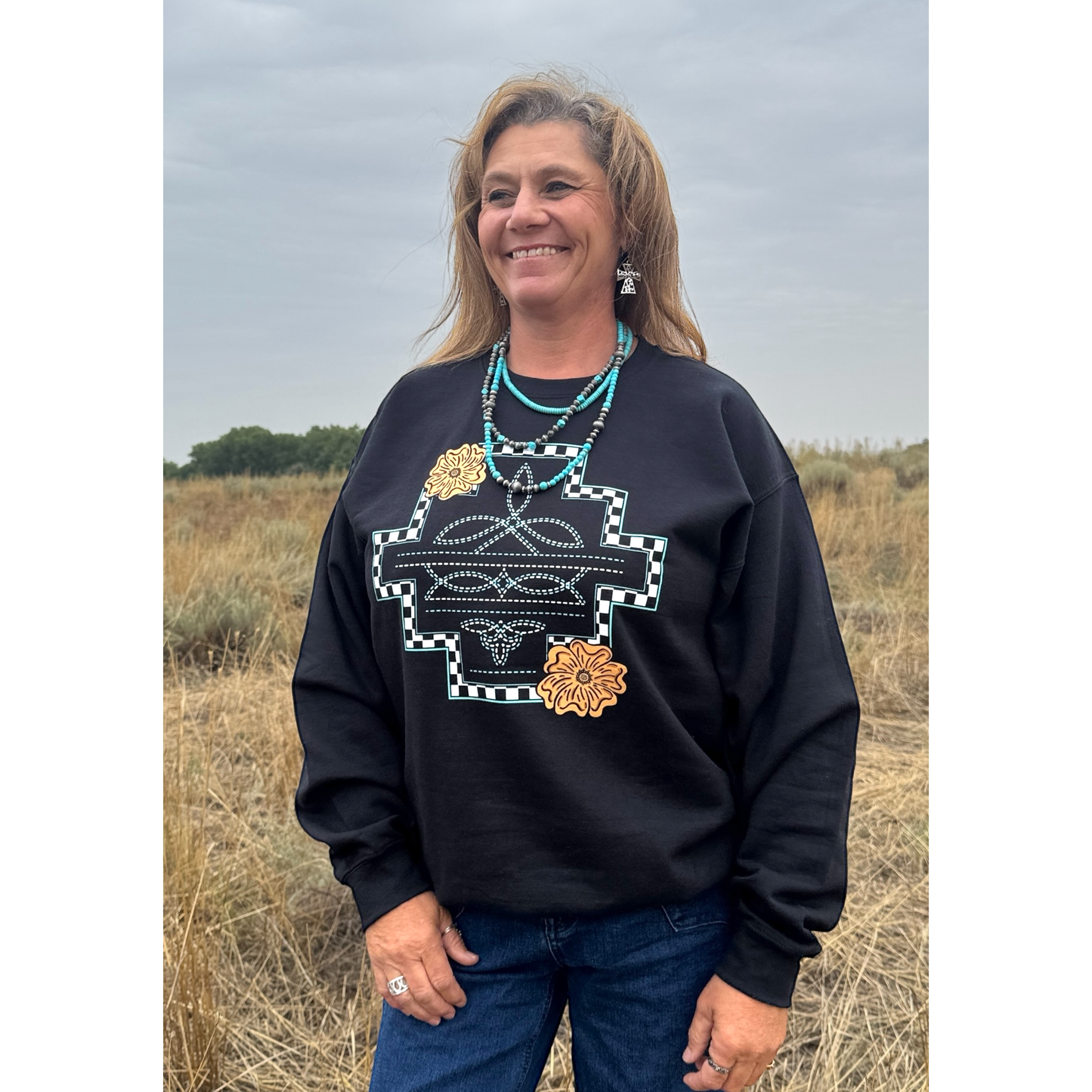Woman standing in a field wearing a western print sweatshirt 